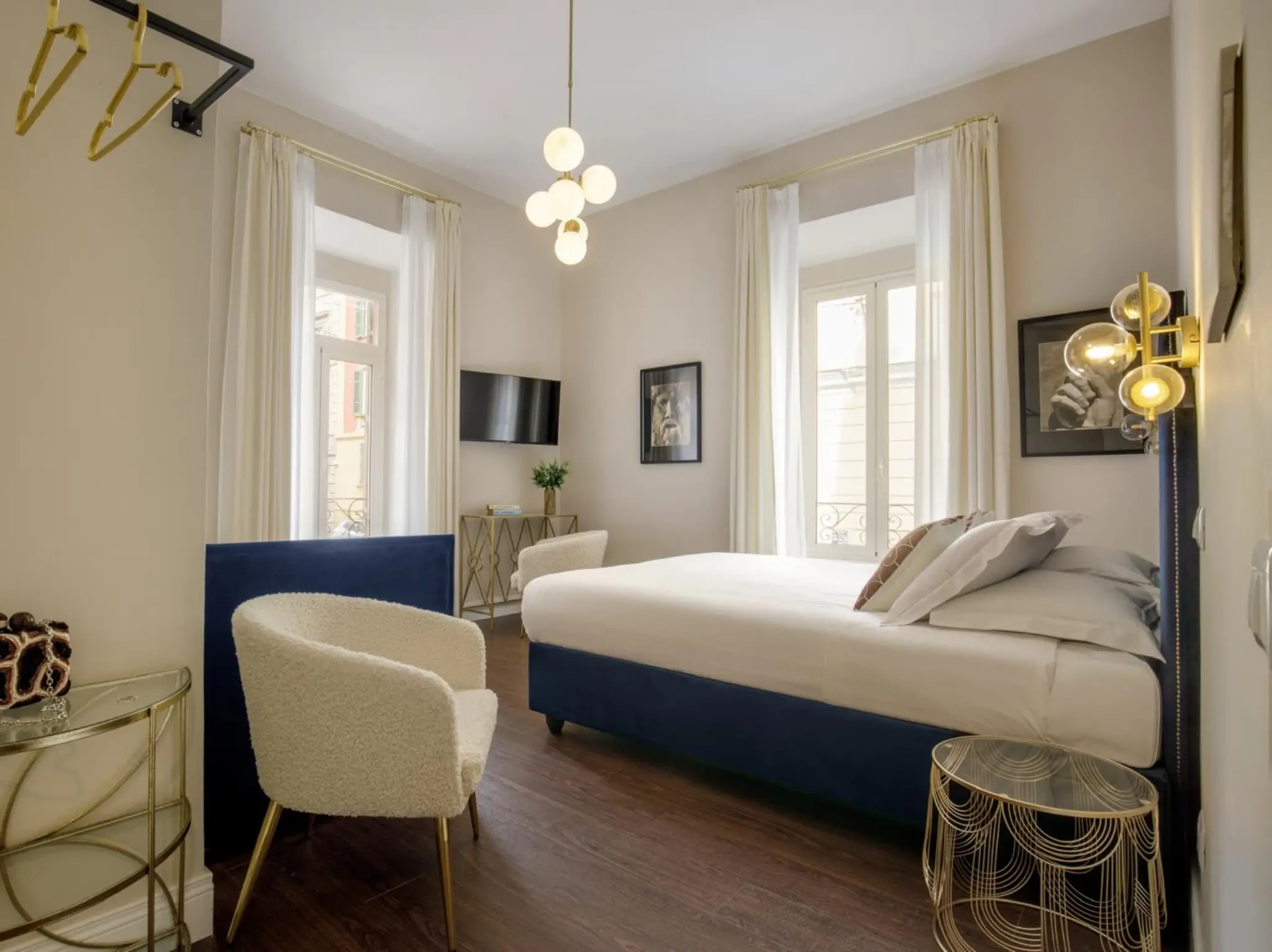 alt="Camera da letto con pavimento effetto legno scuro, pareti beige, letto blu e complementi d'arredo dorati"