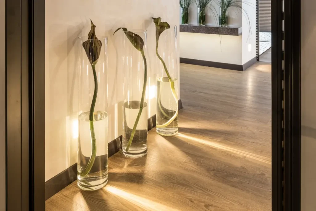 Pavimento effetto legno naturale abbinato a pareti crema, battiscopa scuri e complementi decorativi in vetro