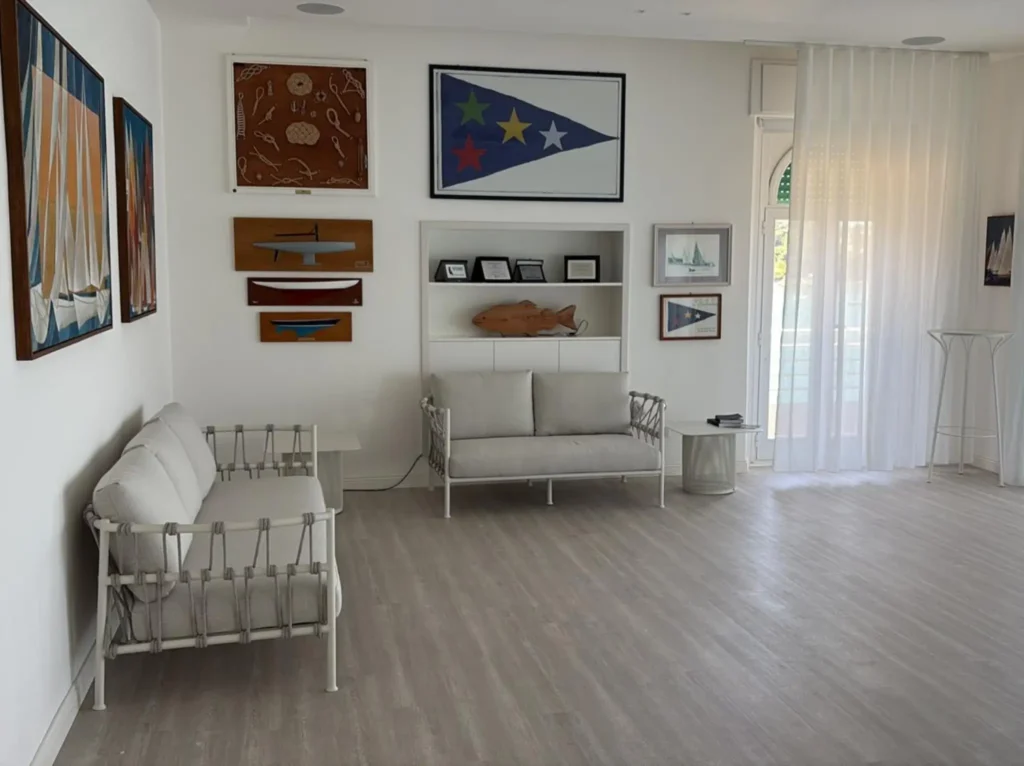Soggiorno luminoso con pavimento effetto legno grigio, pareti bianche, divani chiari e dettagli decorativi blu
